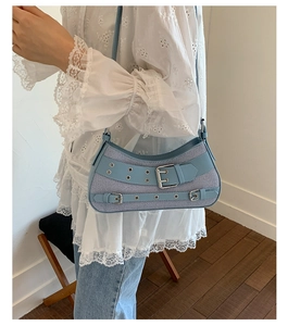 Light blue striped crescent bag with silver eyelets and buckle worn on shoulder