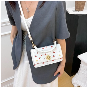 Close-up of white cherry print handbag featuring a golden flower clasp and woven handle
