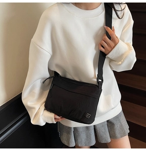 Dettaglio di una borsa a tracolla nera in nylon leggero con logo floreale in argento