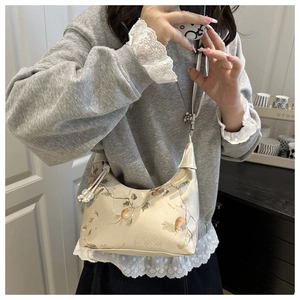 Close-up of champagne satin half-moon bag with elegant floral embroidery and pearl charm