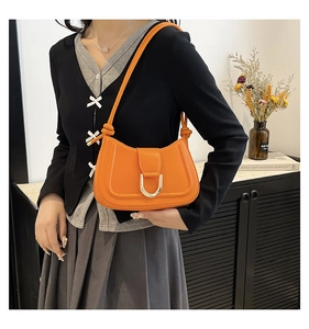 Detail of bright orange shoulder bag featuring a modern gold horseshoe buckle