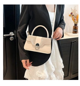 Detail der cremefarbenen Handtasche mit silberner Glitzerklappe und rundem Metallschloss