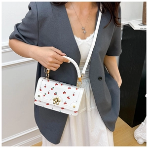 Detail of white handbag with red cherry prints, gold flower clasp and woven handle