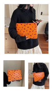 Detail of vibrant orange laptop sleeve featuring a sweet cherry print and metal zippers