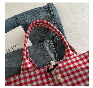 Close-up of red gingham canvas tote with wooden toggle closure and woven rope detail