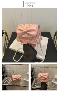 Pink mini crossbody bag with M-pattern print, large bow, and white pearl chain strap