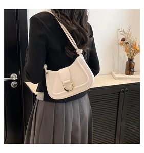 Detail of cream-colored shoulder bag featuring a large gold horseshoe buckle and knot straps