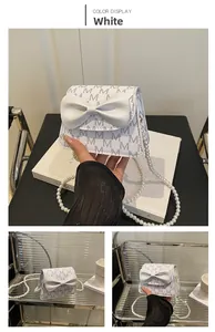 Detail of white crossbody bag with grey monogram pattern, decorative bow and pearl chain strap