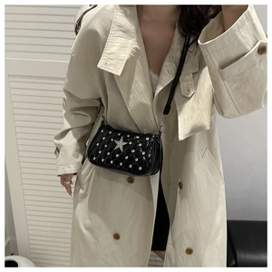 Detail of black quilted crossbody bag with silver studs and a crystal star on a beige coat