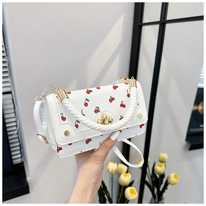 Close-up of white mini crossbody bag with red cherry pattern and woven handle