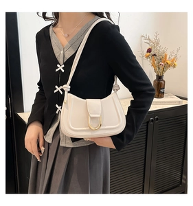 Detail of cream white leather underarm bag featuring a golden U-shaped buckle and knotted strap