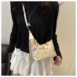 Close-up of bird and floral embroidery details on the beige canvas shoulder bag