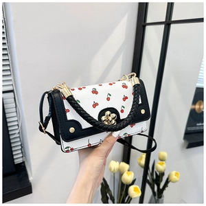 Detail of cute cherry print crossbody bag with golden flower lock and woven handle