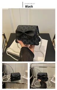 Detail of black bow crossbody bag with letter pattern and pearl chain strap