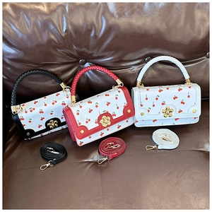 Three textured leather crossbody bags with cherry prints and golden floral clasps on a sofa