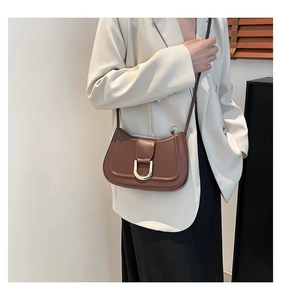 Close-up of minimalist brown saddle bag with gold metal buckle on a white blazer