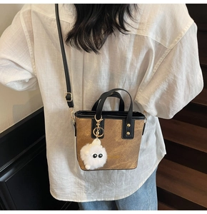 Detail of a brown textured tote bag with black trim and a cute white plush monster charm