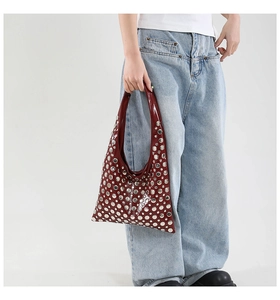 Detail of burgundy patent leather bucket bag with silver rivet studs on a model