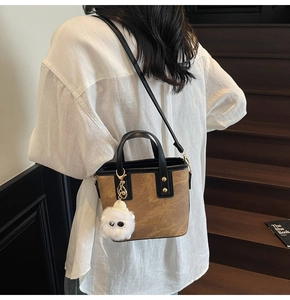 Détail du sac seau marron avec bordure noire et breloque en peluche blanche sur un escalier