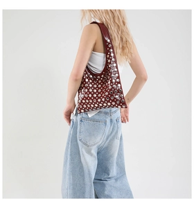 Shoulder view of a wine red bucket bag with silver metal rivets and glossy finish