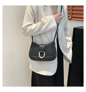 Detail of black leather shoulder bag featuring a golden horseshoe metal buckle and slim strap