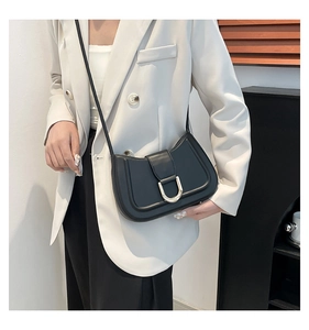 Detail of minimalist black leather crossbody bag with a gold U-shaped metal buckle