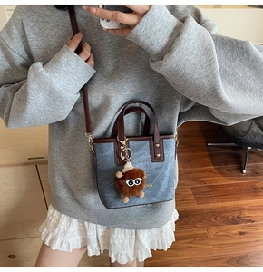 Close-up of gray-blue denim bucket bag with brown leather handles and fuzzy eyeball charm
