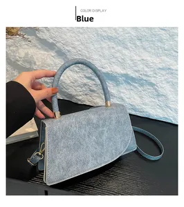 Detail of blue denim textured trapezoid handbag with thick round handle and gold hooks