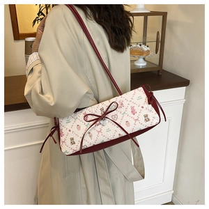 Detail of floral quilted shoulder bag with red bow and heart pendant on model