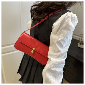 Detail of red baguette shoulder bag featuring elegant gold cylindrical metal clasp lock