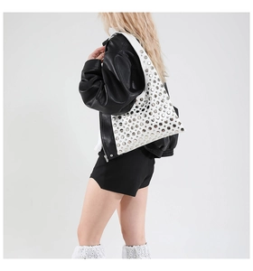 Detail of a white leather shoulder bag featuring dense silver studs and a wide strap