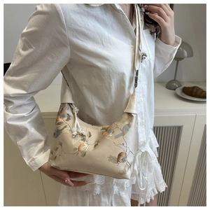 Detail of floral and bird embroidery on beige shoulder bag with knot bead charm
