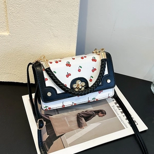 White leather handbag with red cherry print, black woven handle and gold flower lock