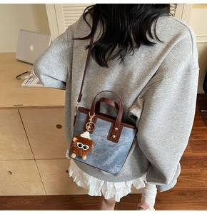 Chic denim and leather tote bag with fashion print and cute plush charm on a model