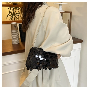 Detail of black sequin crossbody bag with gold chain strap on a trench coat