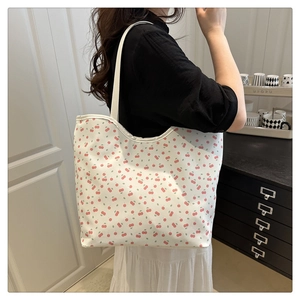 Detail of a large white tote bag with red cherry print worn by a model in a minimal room