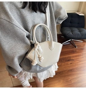 Minimalist white trapezoidal handbag with knotted rope detail, worn by a model in casual attire.