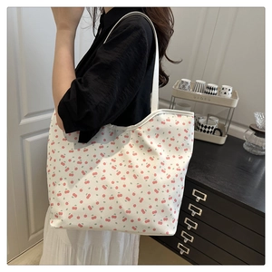 Detail of white shoulder tote bag with red cherry prints shown in a home setting