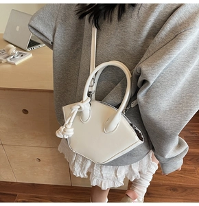 Dettaglio di una borsa a mano bianca minimalista a forma di ventaglio su outfit grigio