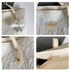 Detailed macro view of embroidered canvas tote bag with leather tag and golden zipper