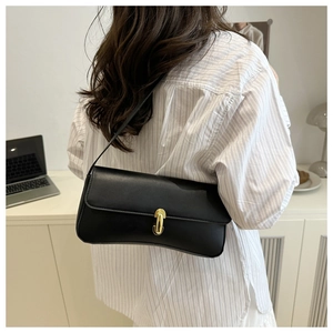 Detail of the chic black underarm bag with a golden oval buckle worn by a model