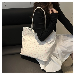 Detail of white canvas tote bag featuring pink floral and bow prints worn on shoulder