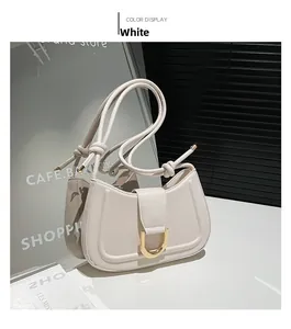 Detail of white leather shoulder bag featuring a large gold buckle and knotted strap design