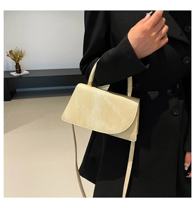 Detail of light beige rectangular crossbody bag with gold hardware on a black coat