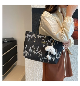 Close-up detail of a black tote bag featuring white zigzag patterns and a cloud charm