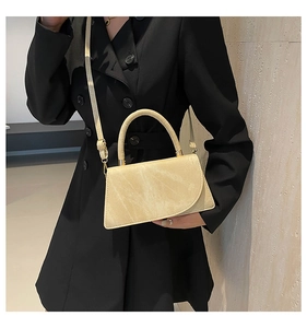 Close-up of cream crossbody bag with suede texture and gold handle on black coat