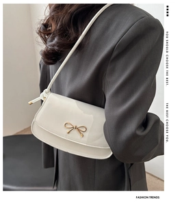 Detailed view of white glossy underarm bag with gold bow clasp on grey blazer
