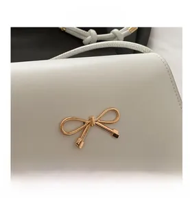 Détail d'un sac en cuir blanc avec un fermoir nœud en métal doré et une bandoulière