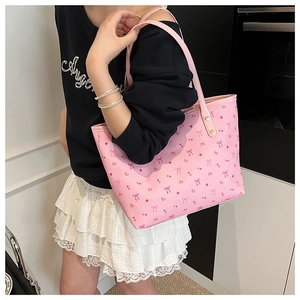 Detail of pink tote bag with red bow pattern worn over the shoulder by a model