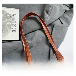 Détail d'une poignée en cuir marron avec coutures sur un sac cabas beige à carreaux